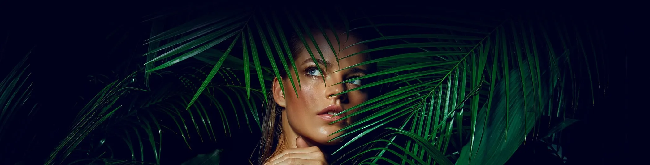 Model with luminous skin surrounded by palm fronds